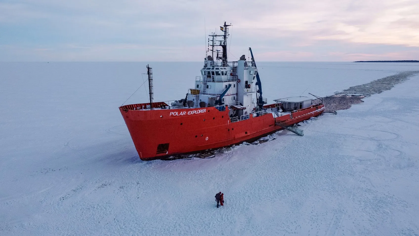 Red icebreaker ship named 'Polar Explorer' breaking through frozen sea ice with two people standing on the ice nearby.